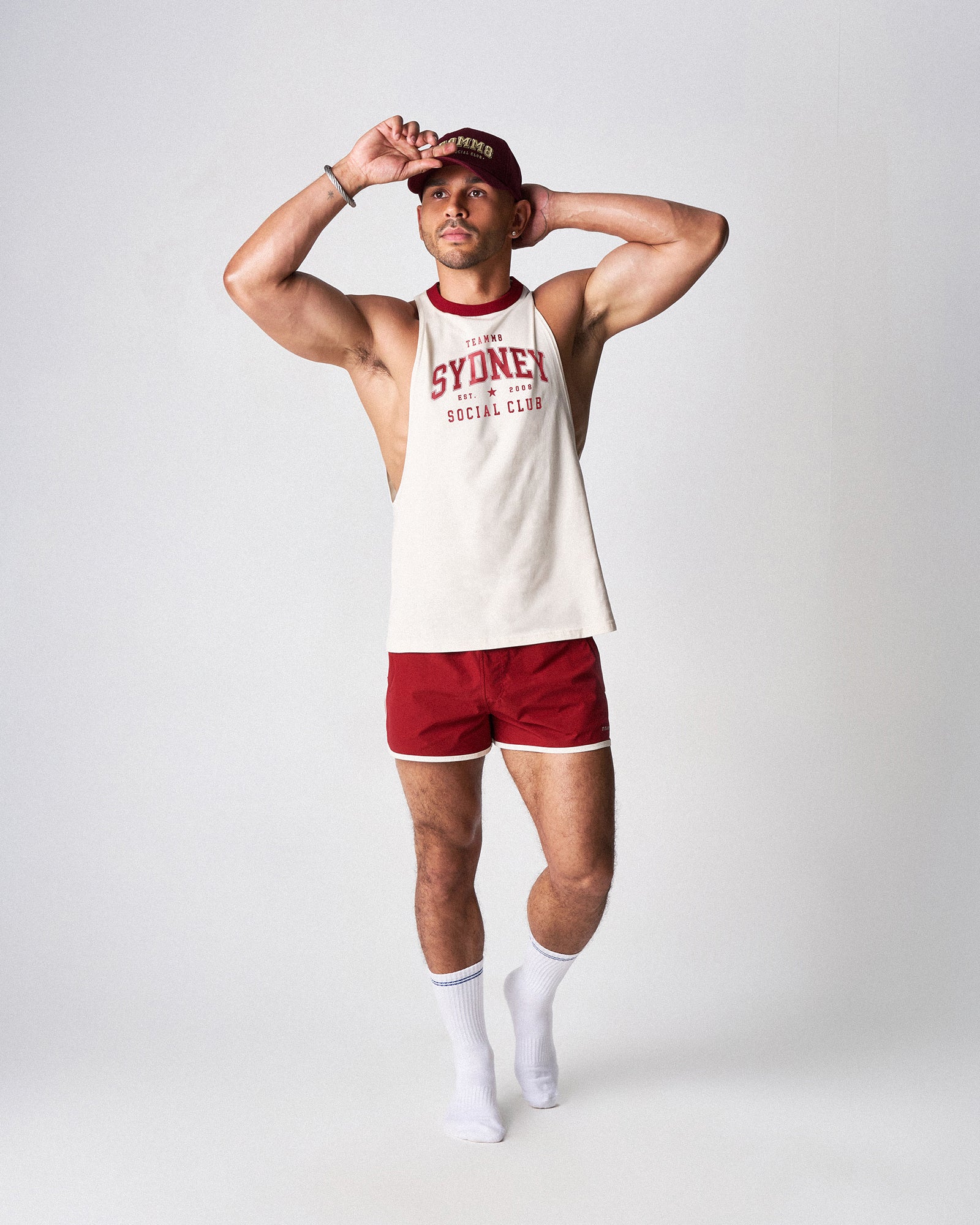 Person wearing a white tank top with red text and red shorts on a plain background