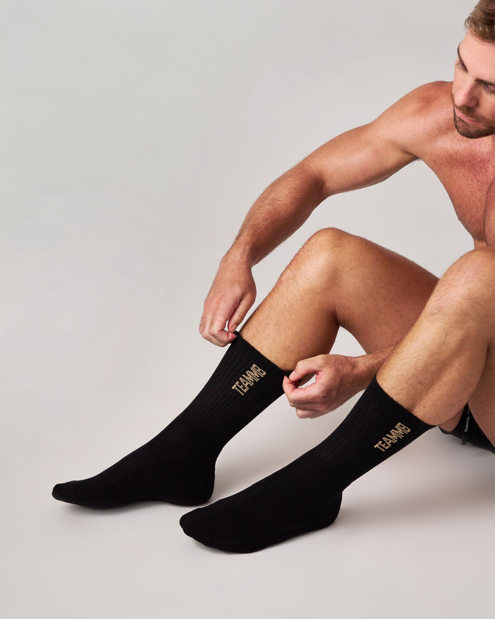Man wearing black socks with visible branding on a plain background